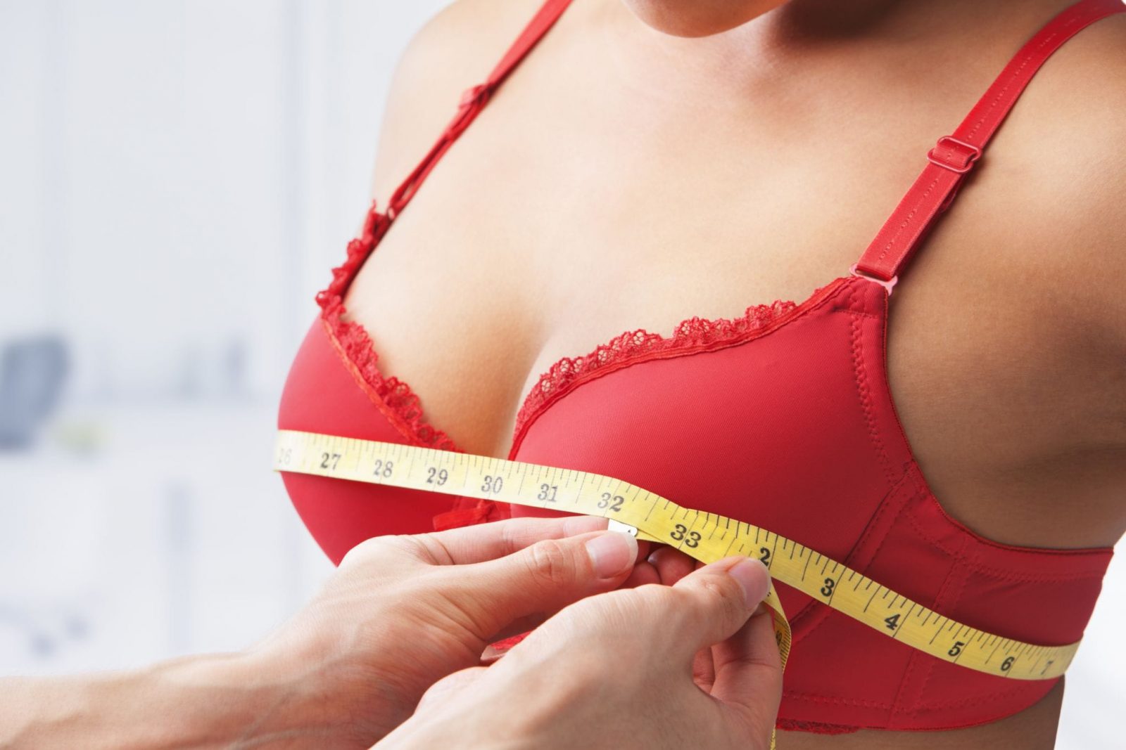 Девушке в красном бюстгальтере измеряют сантиметровой лентой грудь